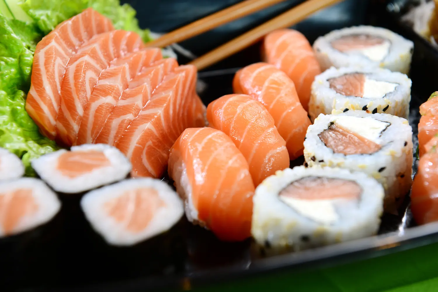 Salmon sashimi and sushi plated on a dark tray